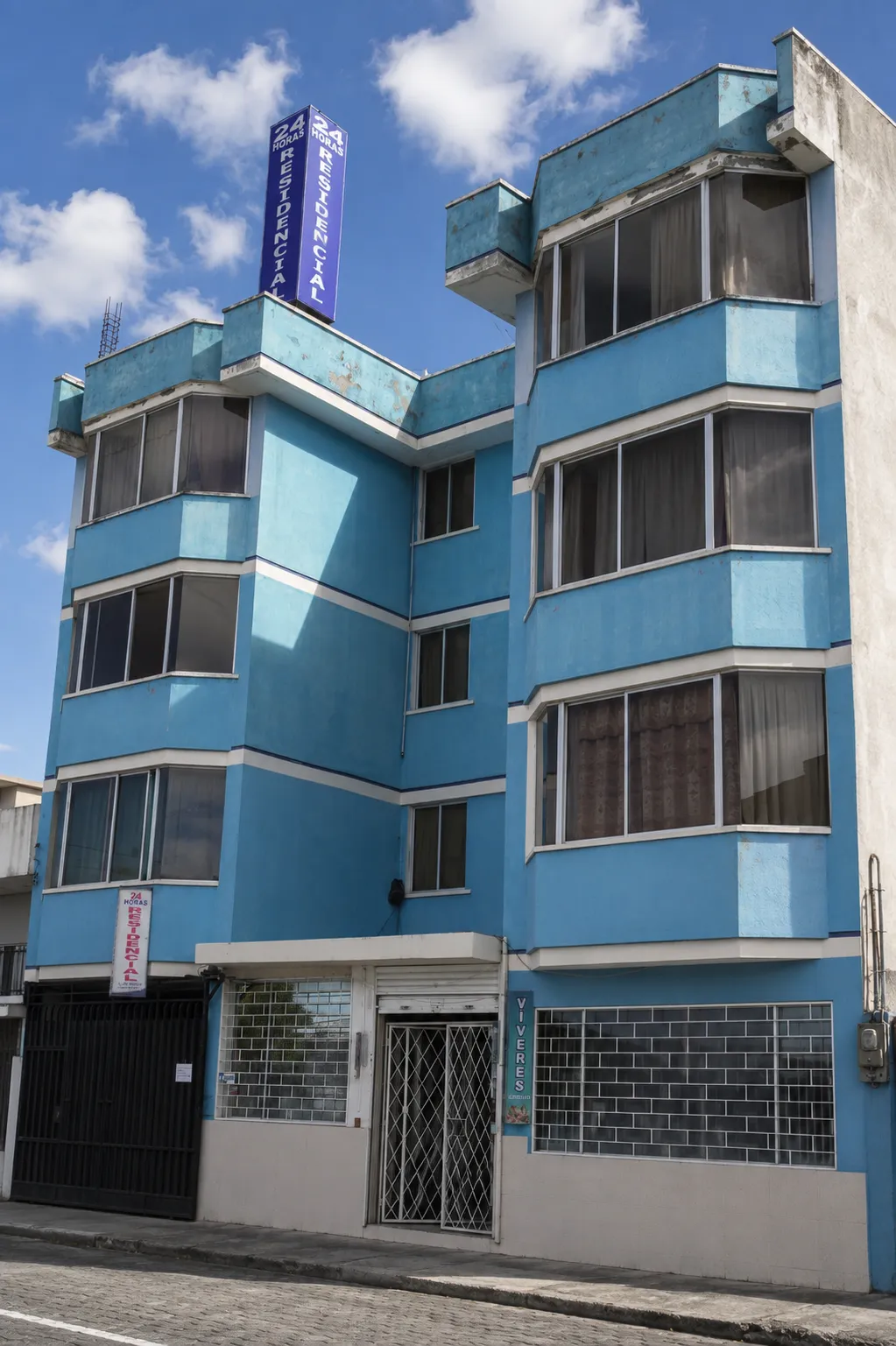 Fachada del edificio azul de la Residencial Best of the Best con el letrero de 24 horas